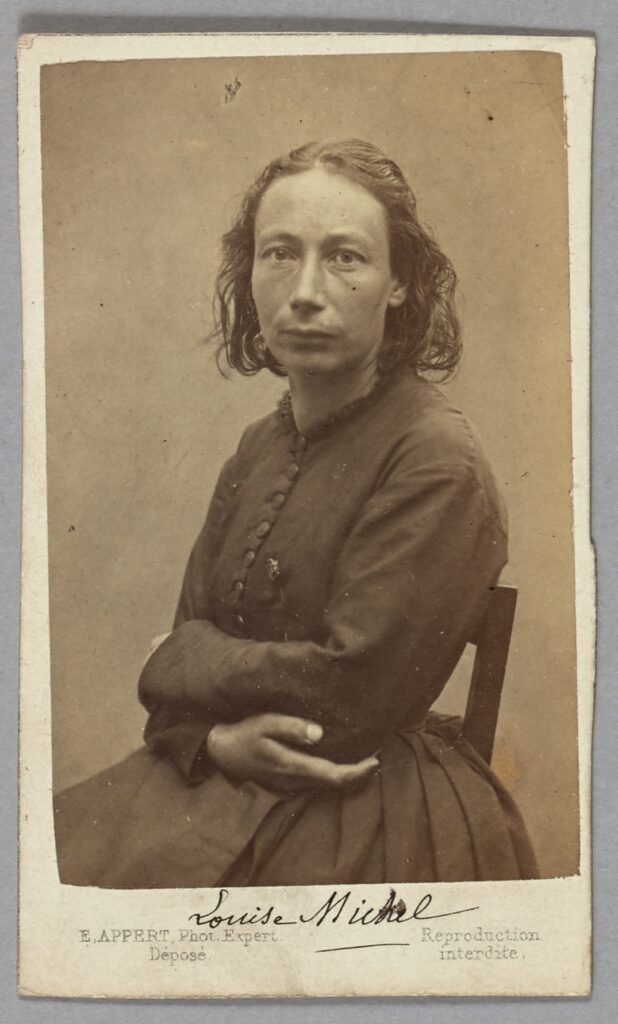 Sepia monochrome portrait of a 19th century woman looking directly at the photographer, with her arms folded